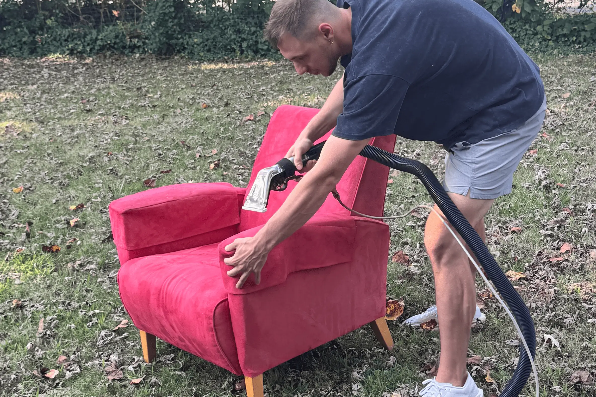 Charlotte Steamers technician performing professional upholstery cleaning on a red accent chair outdoors using steam extraction equipment in Charlotte, NC