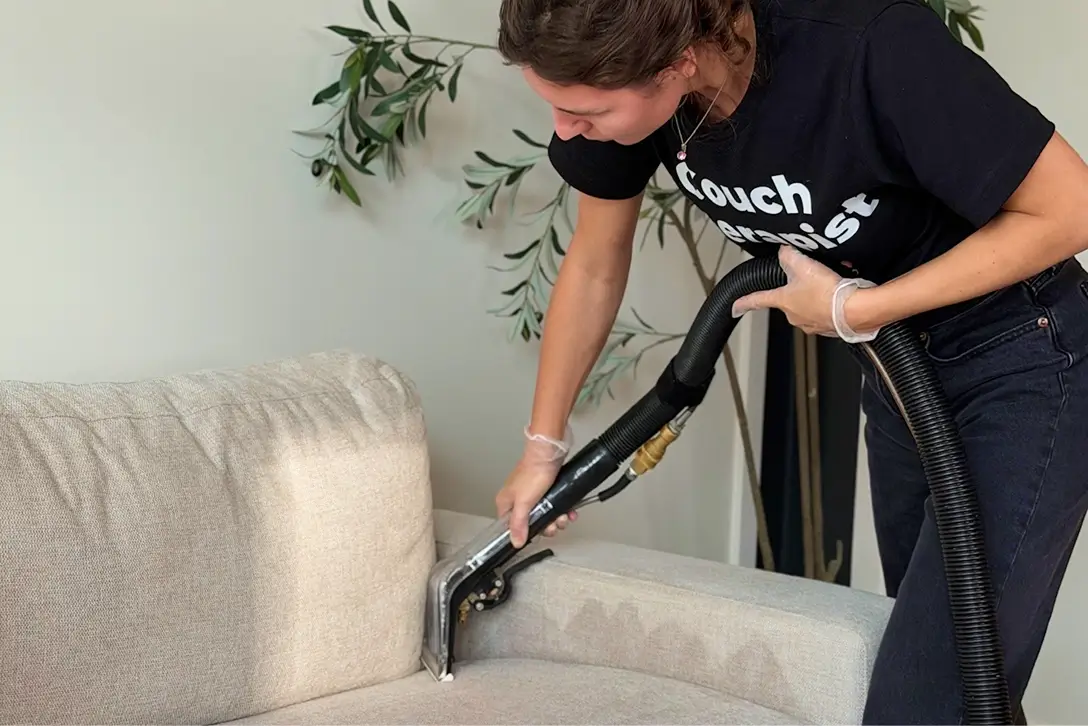 Technician cleaning the arm of a beige fabric couch with an extraction tool during couch cleaning in Dallas, TX