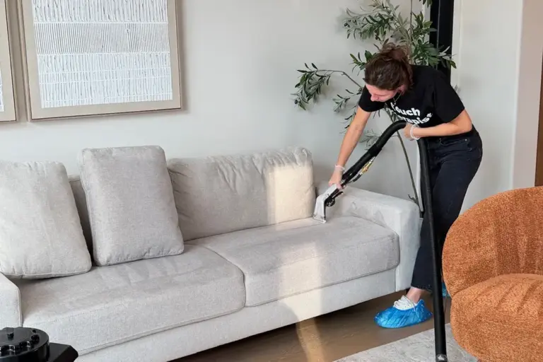 Technician doing couch cleaning on a light gray fabric sofa with a hot water extraction tool