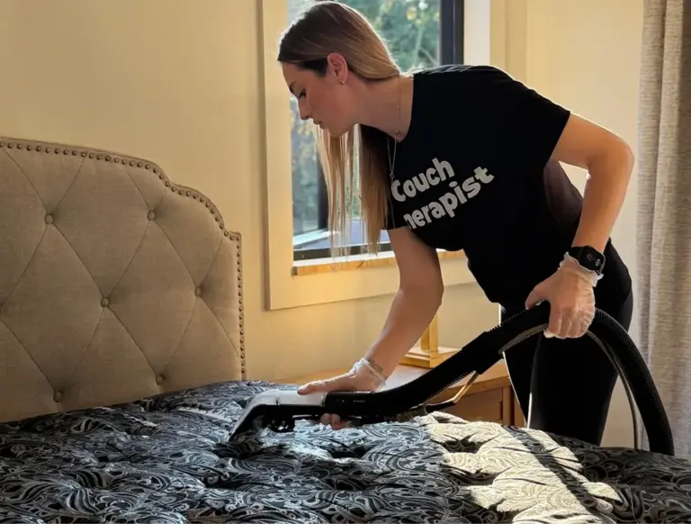 Technician doing professional mattress cleaning on a patterned mattress in a bedroom with an extraction tool