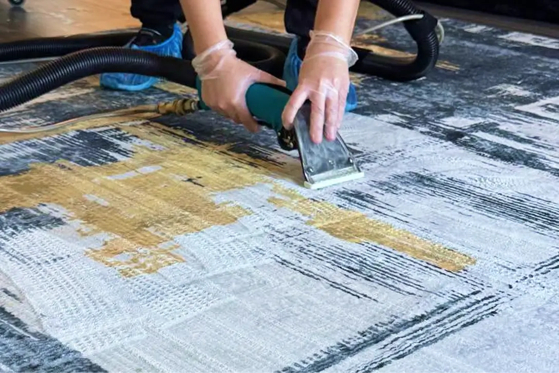 Technician using a hot water extraction tool for professional rug cleaning on a gray and gold area rug