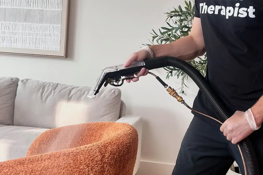 Technician spraying cleaning solution on an orange bouclé armchair during upholstery cleaning in Charlotte, NC