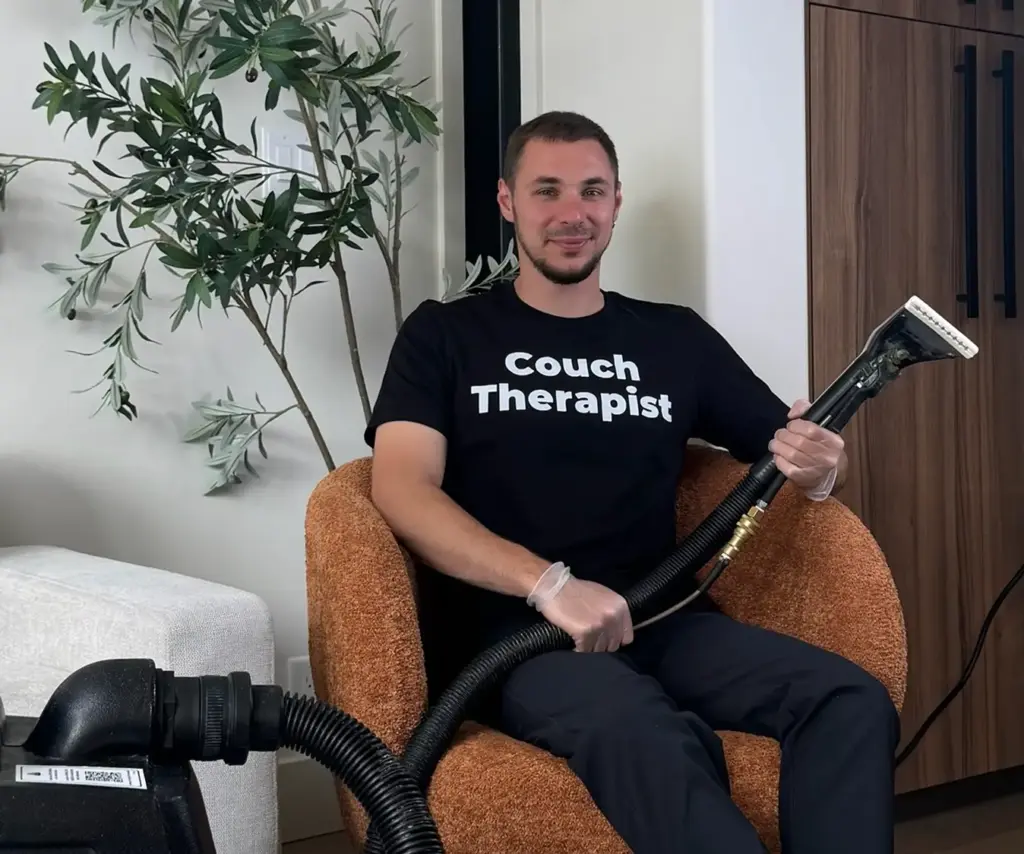 Friendly upholstery cleaning technician sitting in an orange armchair holding a hot water extraction wand