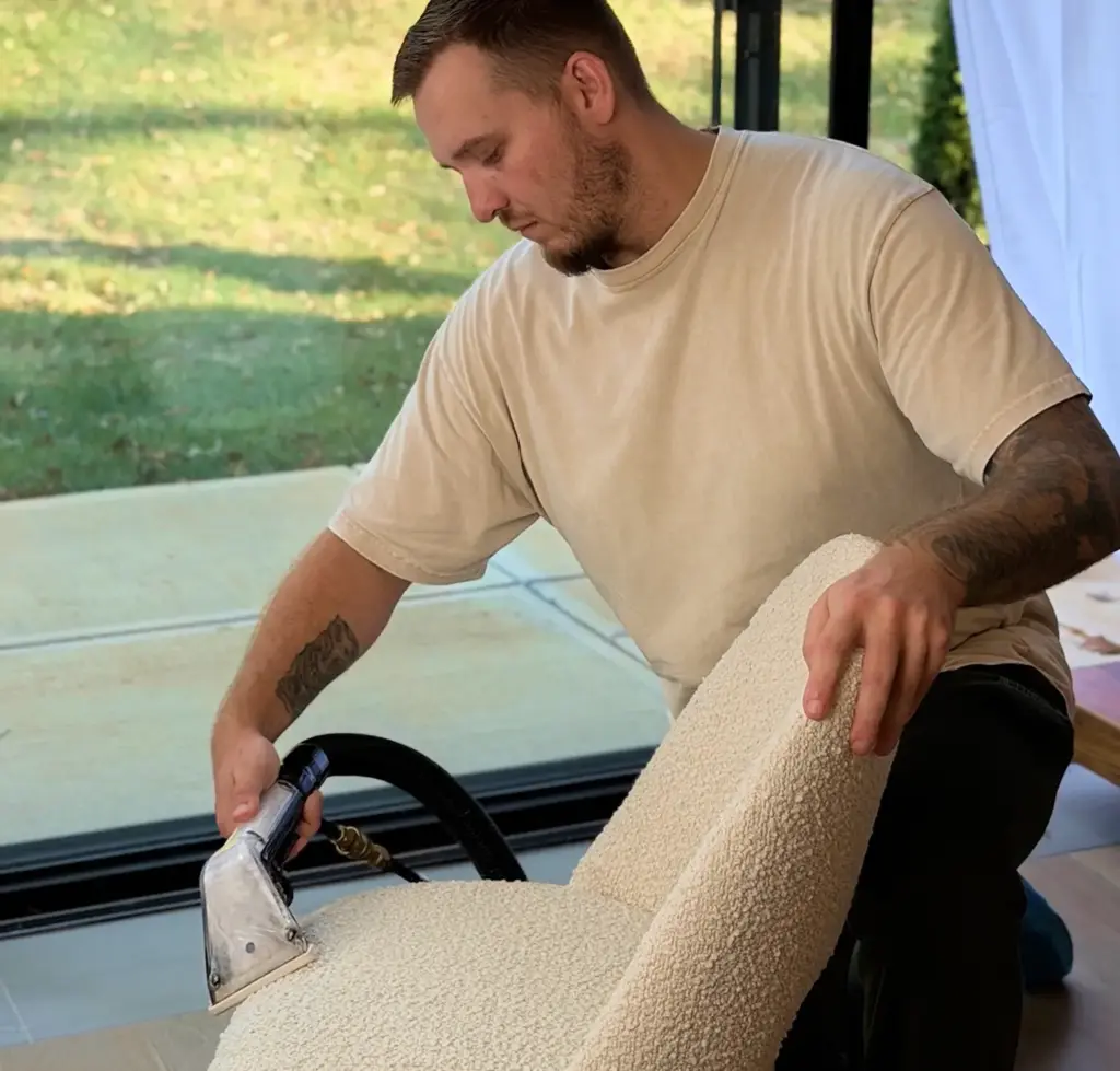 Technician using a hand tool for upholstery fabric cleaning on a cream bouclé accent chair